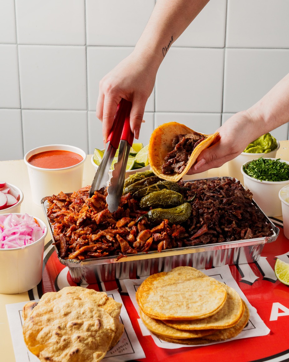 Family order tray of adobada and asada with tortillas, salsas, limes and toppings, served with tongs